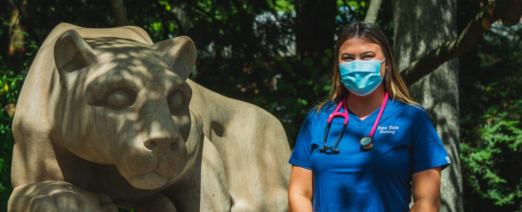 Penn State nurse wearing a mask standing next to the Nittany Lion Shrine